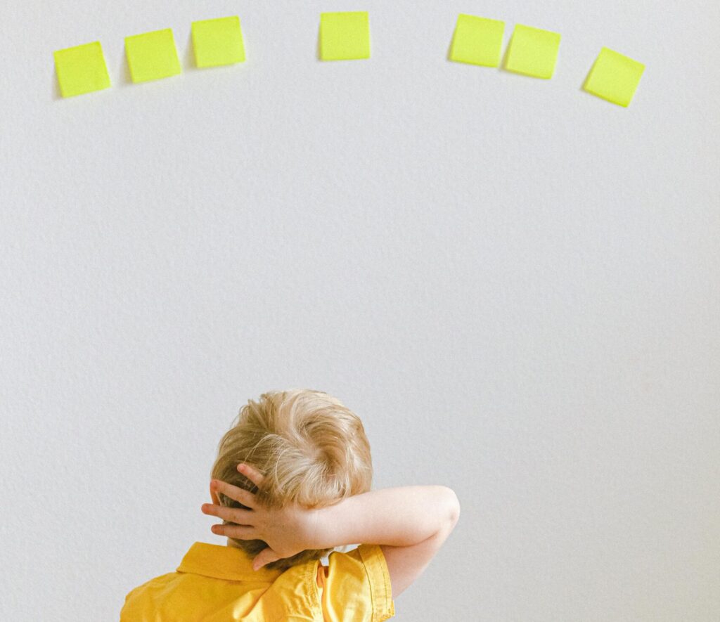 A young boy in a yellow shirt ponders yellow sticky notes on a white wall.